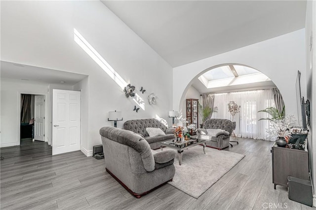 living room featuring a skylight, high vaulted ceiling, and light wood-type flooring