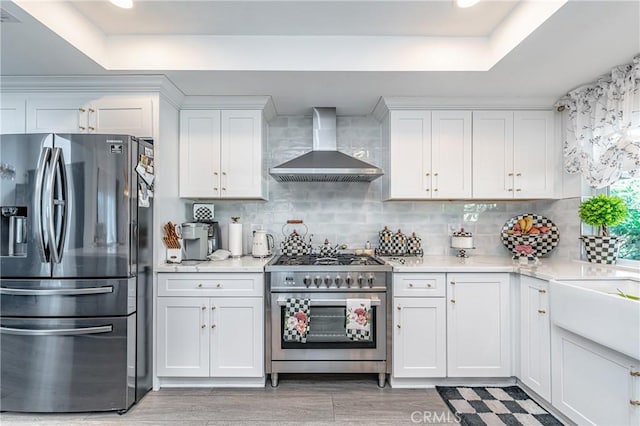 kitchen featuring a tray ceiling, white cabinetry, wall chimney exhaust hood, and stainless steel appliances