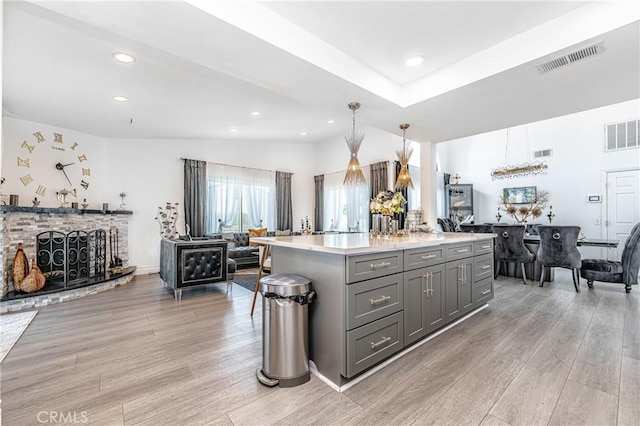 kitchen with gray cabinetry, light hardwood / wood-style flooring, a fireplace, decorative light fixtures, and a kitchen island