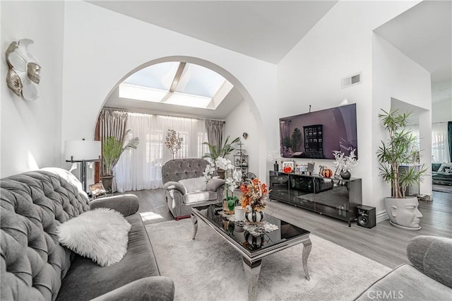 living room with light wood-type flooring, a skylight, and high vaulted ceiling