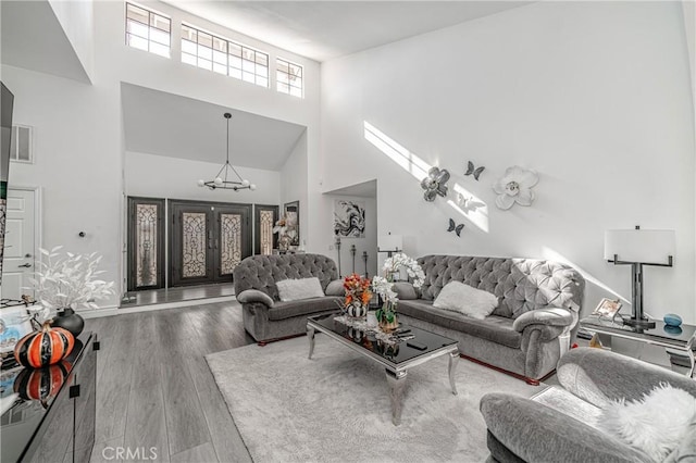 living room featuring wood-type flooring, a towering ceiling, and an inviting chandelier