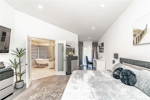 bedroom with ensuite bath, light hardwood / wood-style flooring, and vaulted ceiling