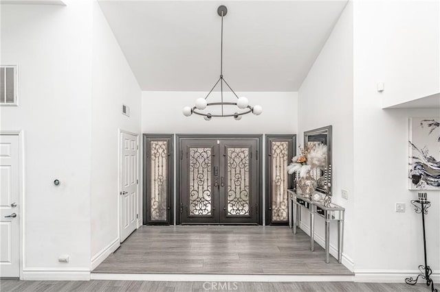 entrance foyer featuring french doors, a towering ceiling, an inviting chandelier, and wood-type flooring