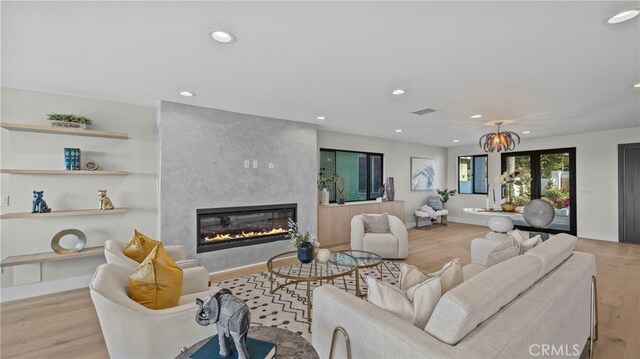 living room with a large fireplace, light hardwood / wood-style floors, and an inviting chandelier