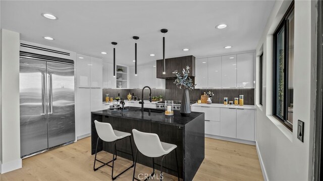 kitchen featuring a center island with sink, hanging light fixtures, light wood-type flooring, appliances with stainless steel finishes, and white cabinetry