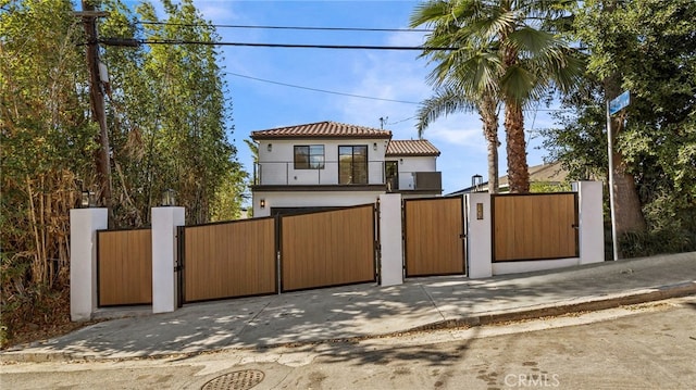 view of front of property featuring a gate, fence, a balcony, and stucco siding