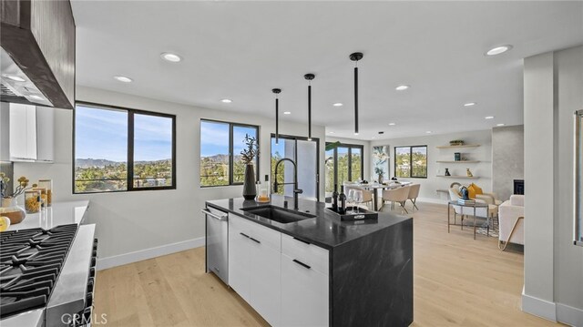 kitchen featuring white cabinets, a center island with sink, sink, wall chimney exhaust hood, and light wood-type flooring