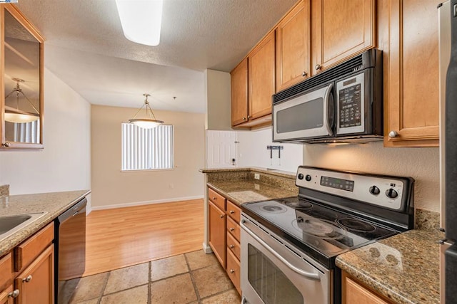 kitchen featuring dark stone counters, a textured ceiling, stainless steel appliances, pendant lighting, and light hardwood / wood-style flooring