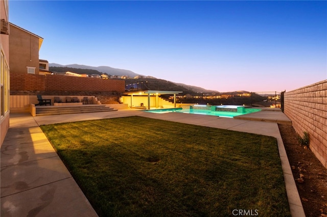 yard at dusk with a mountain view, a patio area, and a pool with hot tub