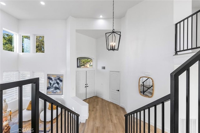 stairs with wood-type flooring, a towering ceiling, and a notable chandelier