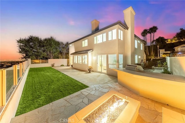 back house at dusk featuring a lawn, area for grilling, a patio, and a fire pit