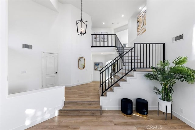 staircase with hardwood / wood-style floors, a towering ceiling, and a notable chandelier