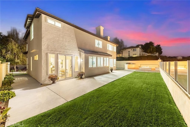 back house at dusk featuring a lawn and a patio