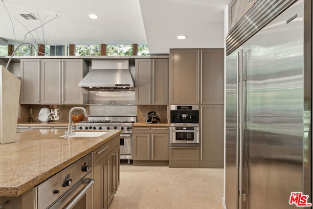 kitchen with sink, wall chimney exhaust hood, decorative backsplash, premium appliances, and light stone counters