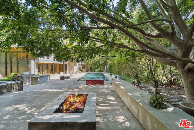 view of pool with an outdoor kitchen, a fire pit, and a patio area