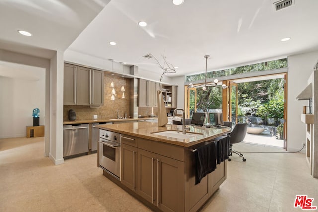 kitchen with light stone countertops, sink, decorative backsplash, a center island with sink, and appliances with stainless steel finishes