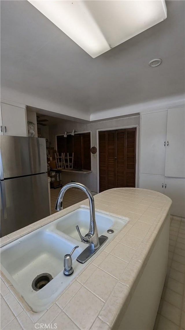 kitchen featuring stainless steel refrigerator, white cabinetry, sink, tile countertops, and light tile patterned flooring