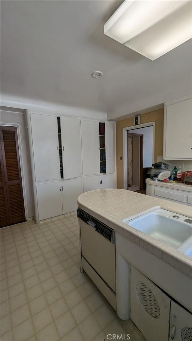 kitchen featuring backsplash, sink, dishwasher, white cabinetry, and tile counters