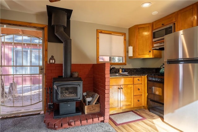 kitchen with stainless steel appliances, a wood stove, plenty of natural light, and light hardwood / wood-style flooring