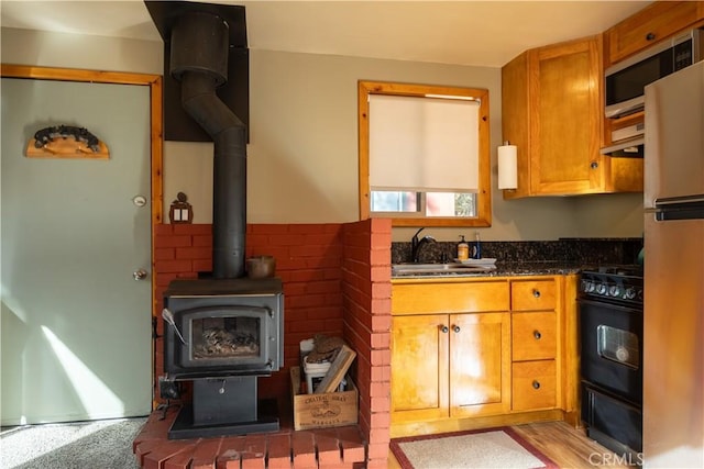 kitchen with light wood-type flooring, a wood stove, sink, and appliances with stainless steel finishes