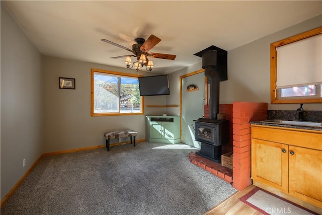 carpeted living room featuring ceiling fan, a wood stove, and sink