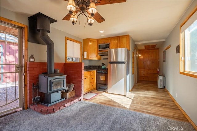 kitchen featuring appliances with stainless steel finishes, light wood-type flooring, radiator, ceiling fan, and a wood stove