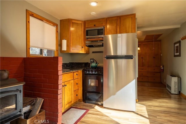 kitchen with heating unit, light hardwood / wood-style flooring, dark stone countertops, and stainless steel appliances