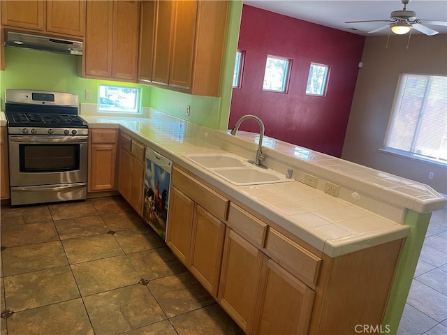 kitchen with dishwasher, sink, stainless steel gas range oven, tile countertops, and kitchen peninsula