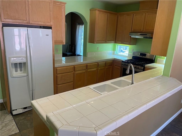 kitchen featuring kitchen peninsula, stainless steel gas range oven, tile counters, and white fridge with ice dispenser