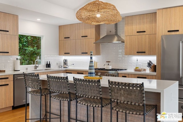 kitchen with appliances with stainless steel finishes, wall chimney exhaust hood, a breakfast bar, and a kitchen island