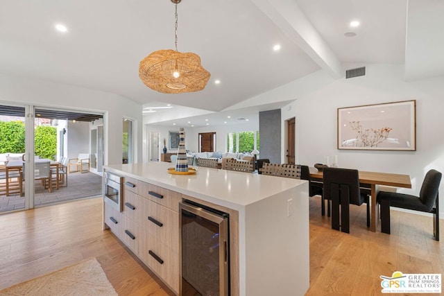 kitchen featuring wine cooler, stainless steel microwave, a kitchen island, pendant lighting, and light hardwood / wood-style floors