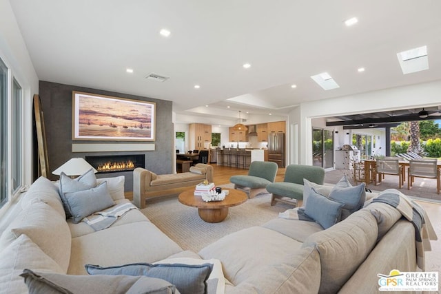 living room with a skylight, a large fireplace, and light wood-type flooring