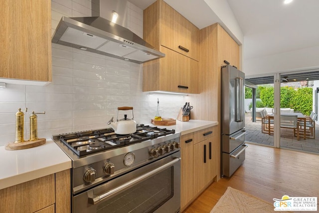 kitchen with tasteful backsplash, premium appliances, wall chimney exhaust hood, and light wood-type flooring