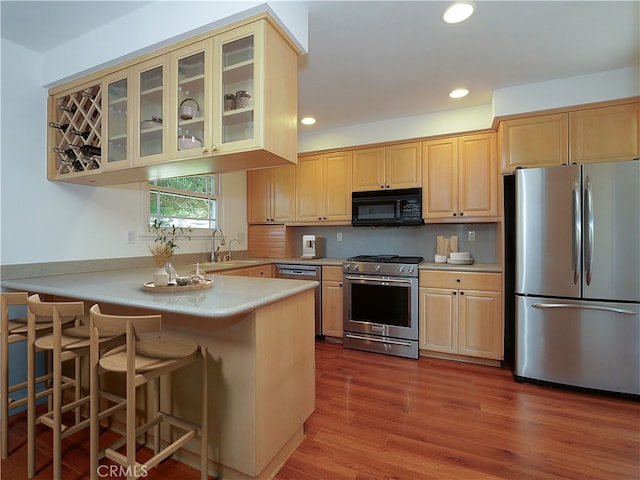 kitchen featuring sink, light hardwood / wood-style flooring, kitchen peninsula, a breakfast bar area, and appliances with stainless steel finishes