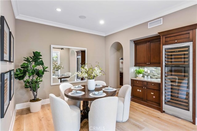 dining space with light hardwood / wood-style floors, beverage cooler, and crown molding