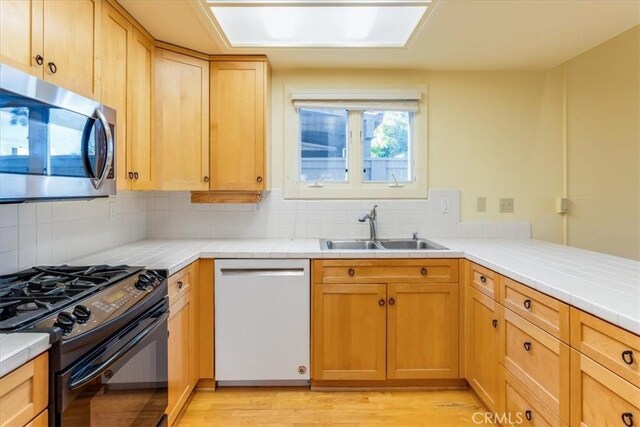 kitchen featuring sink, light brown cabinets, backsplash, appliances with stainless steel finishes, and light wood-type flooring