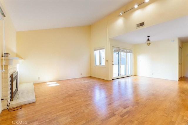 unfurnished living room with light hardwood / wood-style flooring, track lighting, and a brick fireplace