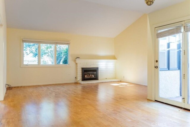 unfurnished living room with a wealth of natural light, light hardwood / wood-style floors, lofted ceiling, and a brick fireplace