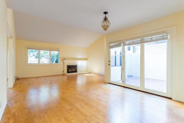 unfurnished living room featuring an inviting chandelier, light wood-type flooring, a fireplace, and vaulted ceiling