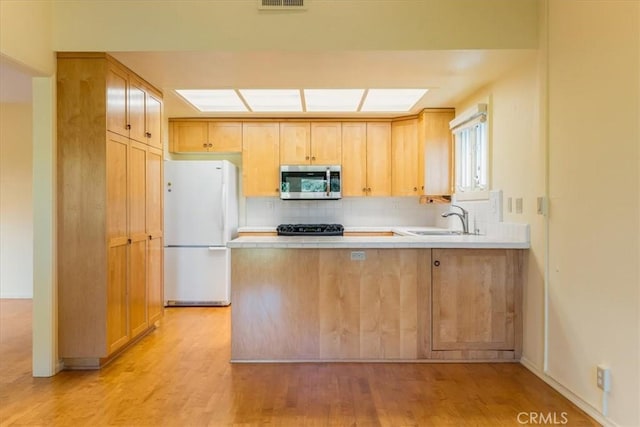 kitchen with light brown cabinets, sink, light hardwood / wood-style flooring, white fridge, and kitchen peninsula