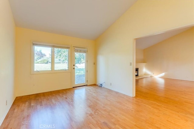 spare room with light wood-type flooring, high vaulted ceiling, and a brick fireplace