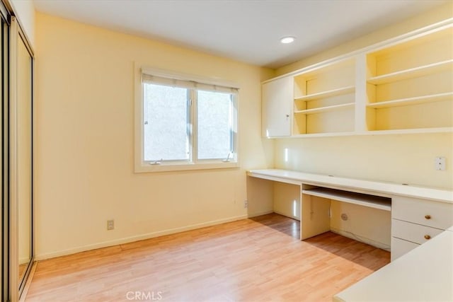 unfurnished office featuring built in desk and light hardwood / wood-style floors