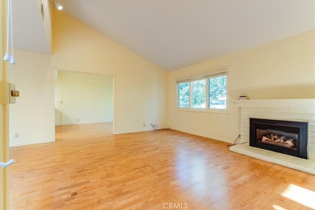 unfurnished living room featuring hardwood / wood-style flooring, high vaulted ceiling, and a tiled fireplace