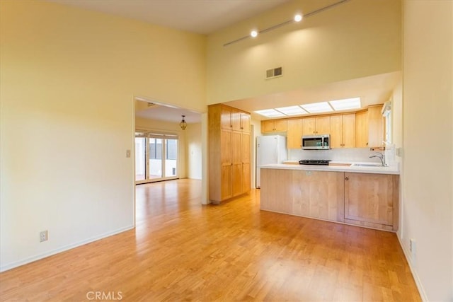 kitchen with kitchen peninsula, light wood-type flooring, light brown cabinets, white refrigerator, and a high ceiling