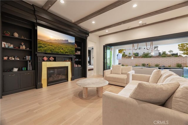 interior space featuring a tiled fireplace, beam ceiling, and light wood-type flooring