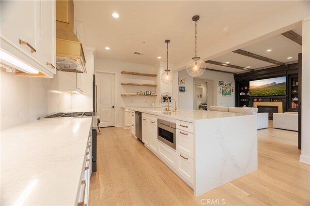 kitchen featuring decorative light fixtures, a center island with sink, stainless steel appliances, beam ceiling, and white cabinets