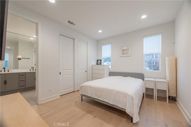 bedroom featuring connected bathroom, sink, a closet, and light wood-type flooring