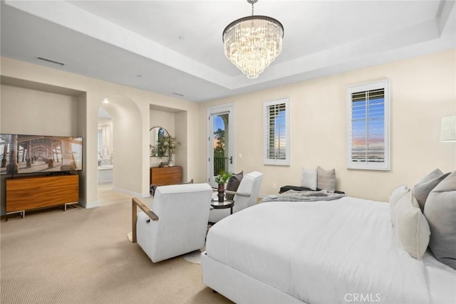 carpeted bedroom featuring a notable chandelier, a raised ceiling, and connected bathroom