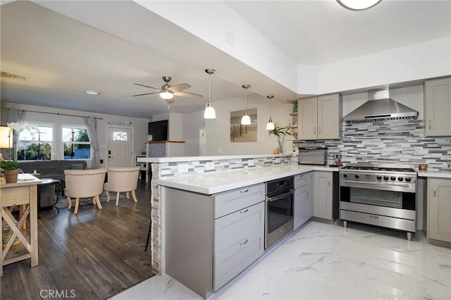 kitchen with appliances with stainless steel finishes, decorative backsplash, kitchen peninsula, and wall chimney range hood