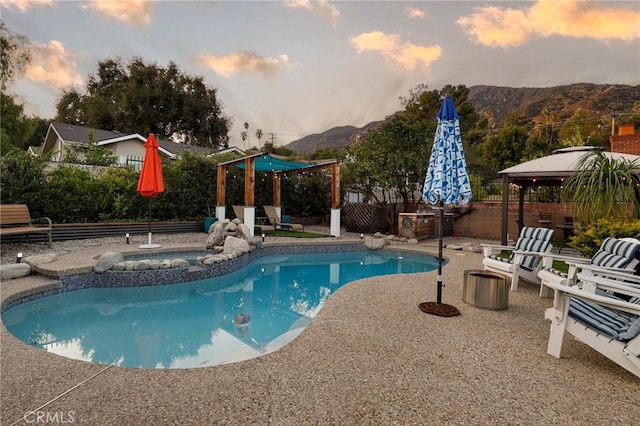 pool at dusk featuring a patio area, a gazebo, a mountain view, and an in ground hot tub